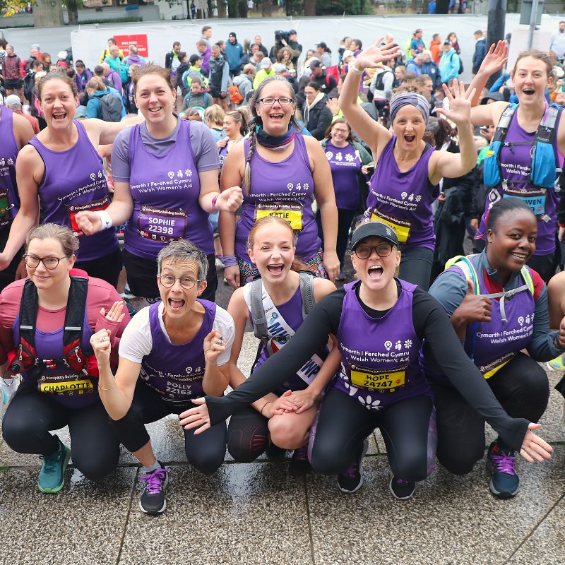 Group of 10 females runners cheering, wearing WWA purple running vests.
